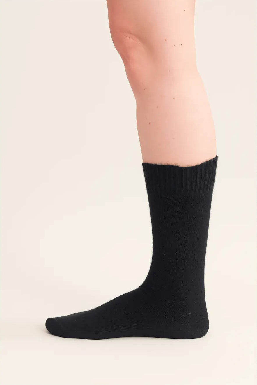 half british alpaca everyday sock in black, worn side-on to highlight the fine knit texture and classic mid-calf length against a soft beige background